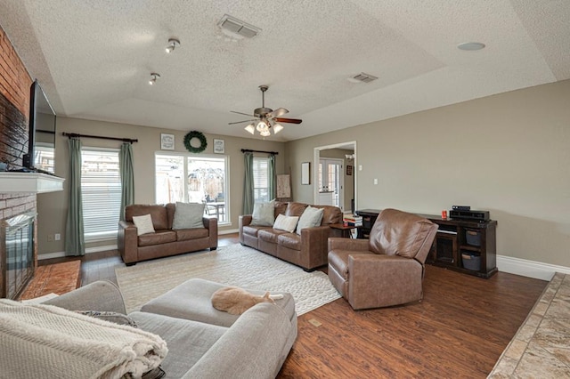 living area with visible vents, baseboards, vaulted ceiling, a fireplace, and wood finished floors