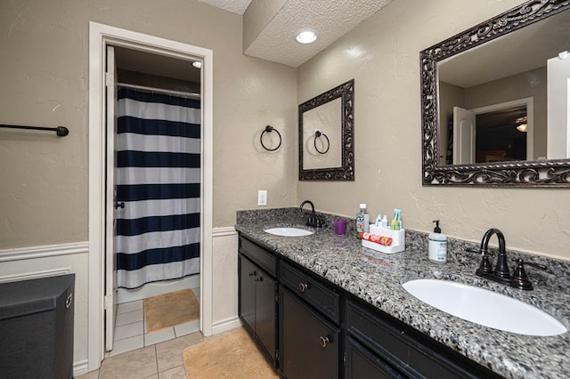 full bath featuring a textured ceiling, tile patterned floors, double vanity, and a sink