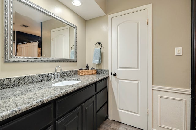 full bathroom with vanity, a wainscoted wall, wood finished floors, and visible vents