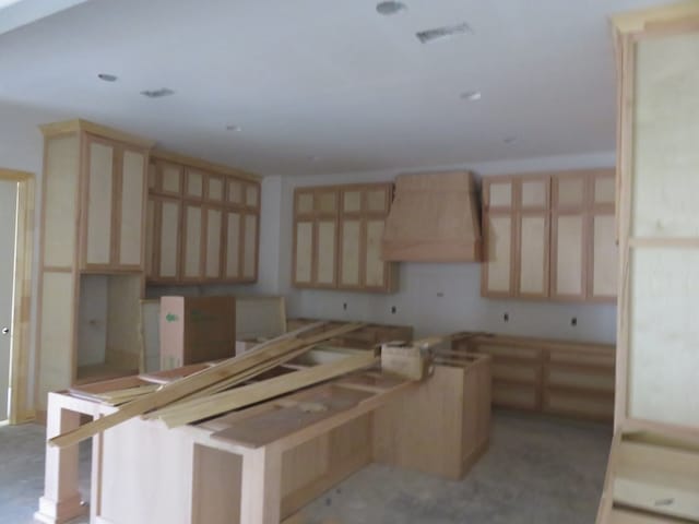 kitchen featuring wall chimney range hood and light brown cabinets