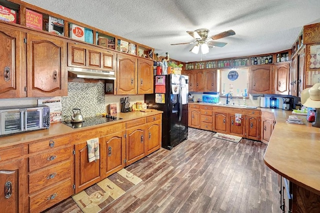 kitchen featuring dark wood-type flooring, black appliances, sink, ceiling fan, and a textured ceiling