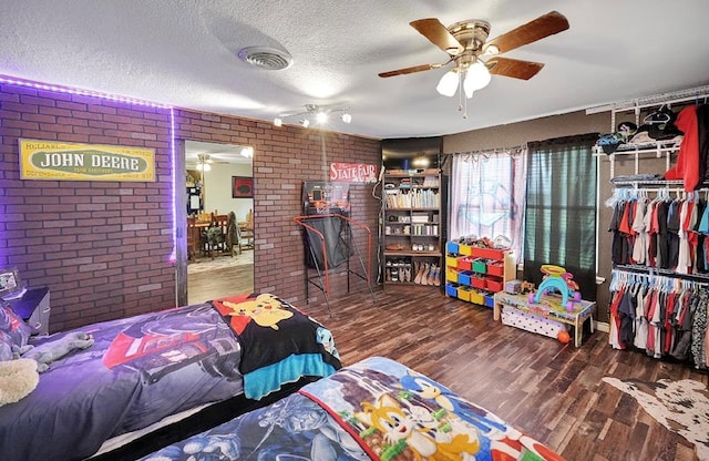 bedroom featuring hardwood / wood-style flooring, ceiling fan, a textured ceiling, brick wall, and a closet