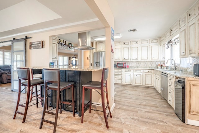 kitchen with sink, stainless steel appliances, a barn door, ventilation hood, and a breakfast bar