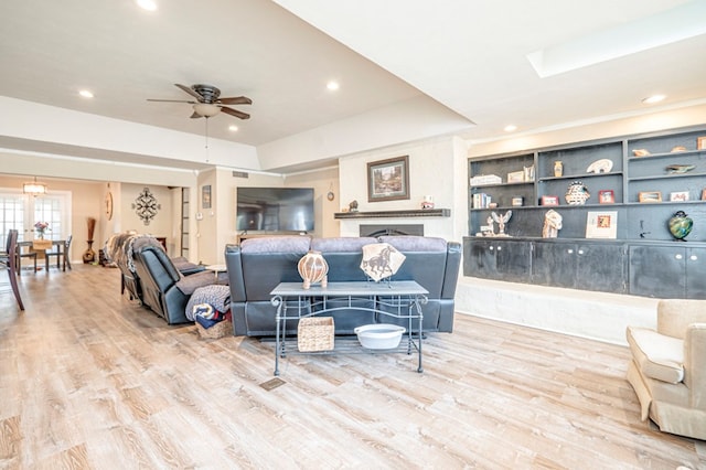 living room featuring a skylight, ceiling fan, light hardwood / wood-style flooring, and built in shelves