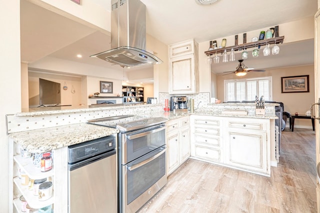 kitchen featuring light stone countertops, ceiling fan, kitchen peninsula, island exhaust hood, and range with two ovens