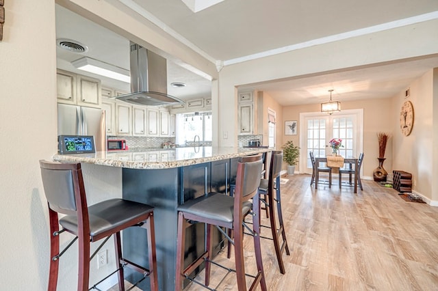 kitchen with stainless steel refrigerator, light stone countertops, backsplash, light hardwood / wood-style floors, and island range hood