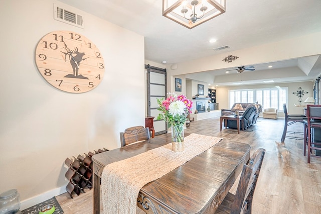 dining room featuring hardwood / wood-style floors, ceiling fan with notable chandelier, and a raised ceiling