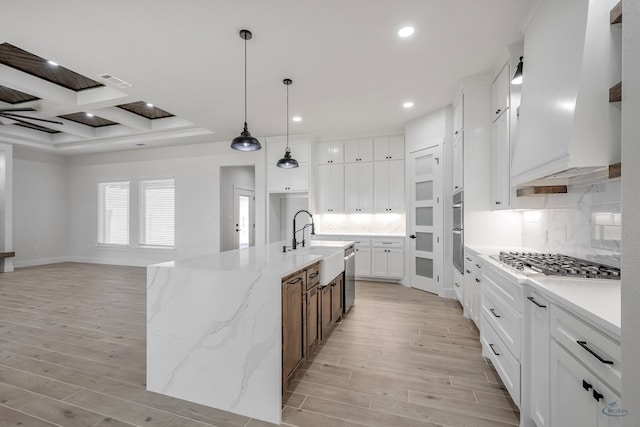 kitchen with premium range hood, white cabinetry, an island with sink, and light wood-type flooring