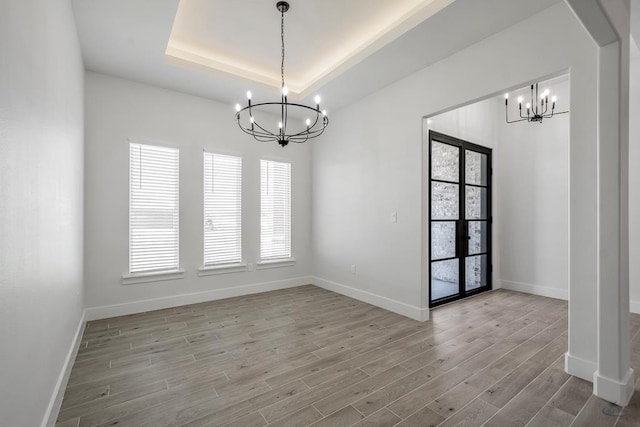 empty room with light wood-type flooring, french doors, a tray ceiling, and a chandelier