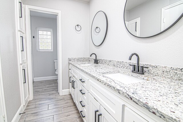 full bath featuring double vanity, baseboards, wood tiled floor, and a sink