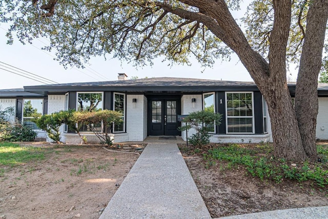 view of front of property with french doors, brick siding, and a chimney