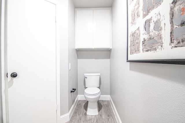 bathroom with toilet, baseboards, and wood finished floors