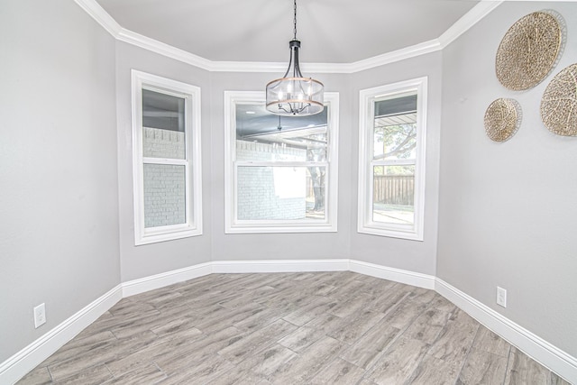 unfurnished dining area featuring light wood-style flooring, an inviting chandelier, crown molding, and baseboards