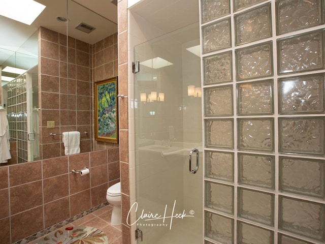 bathroom with a skylight, tile patterned flooring, toilet, a shower with door, and tile walls