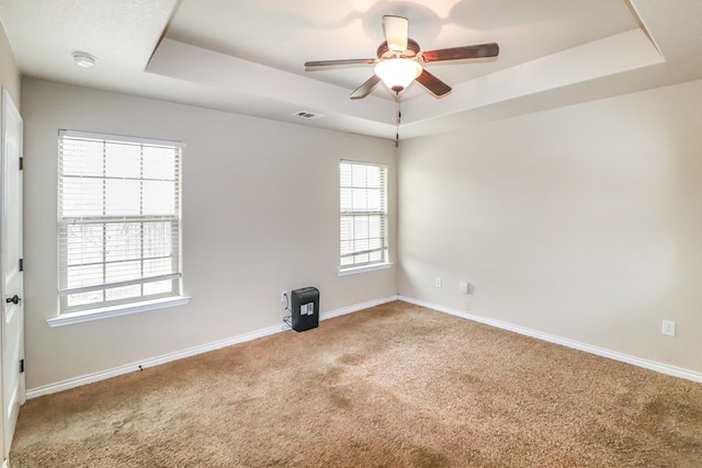 empty room featuring ceiling fan, a raised ceiling, and carpet floors