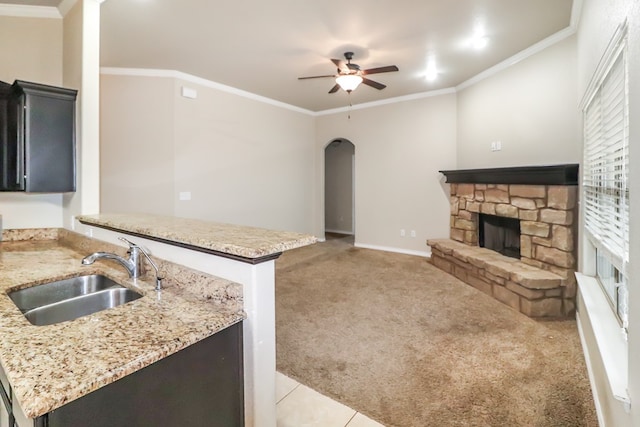 kitchen featuring a stone fireplace, sink, ceiling fan, crown molding, and light carpet