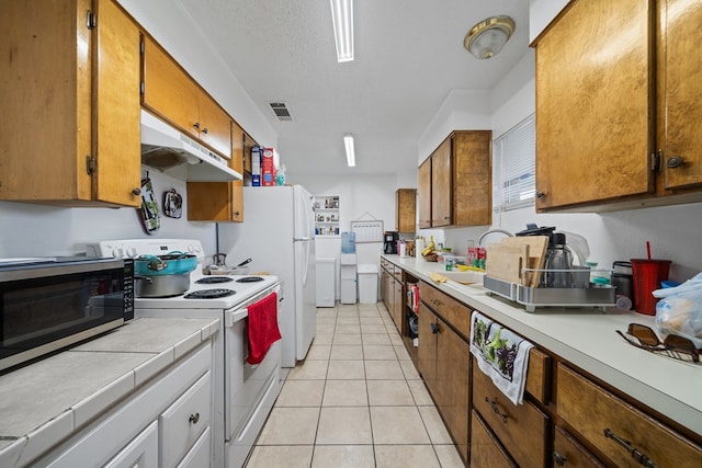 704 Birdwell Ln, Big Spring, TX 79720 - kitchen featuring white appliances, under cabinet range hood, brown cabinets, and light tile patterned floors