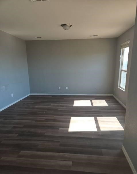 unfurnished room featuring dark wood-style flooring, visible vents, and baseboards