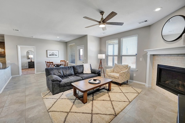 tiled living room featuring ceiling fan and a brick fireplace