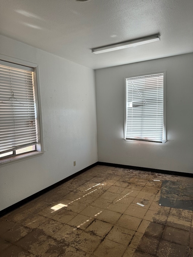 unfurnished room with baseboards and a textured ceiling