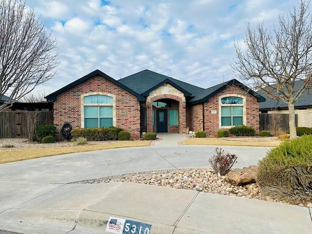 ranch-style home with brick siding, roof with shingles, and fence