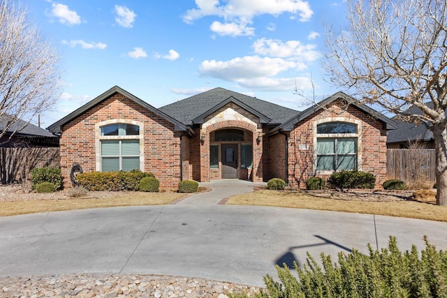 view of front of property featuring a shingled roof, brick siding, and fence