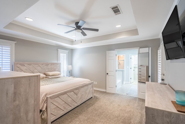 carpeted bedroom featuring a tray ceiling, ensuite bath, ceiling fan, and crown molding