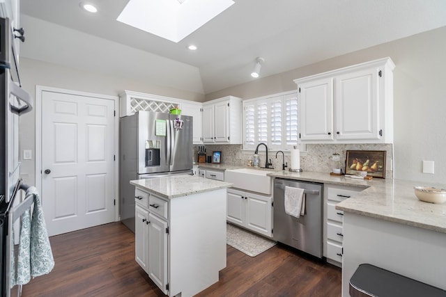 kitchen with light stone countertops, white cabinetry, sink, stainless steel appliances, and lofted ceiling with skylight