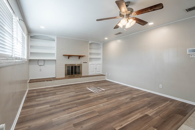 unfurnished living room featuring built in shelves, ceiling fan, a fireplace, and dark wood-type flooring