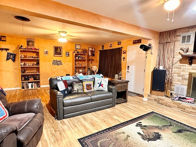 living room with beamed ceiling, wood-type flooring, a large fireplace, and ceiling fan