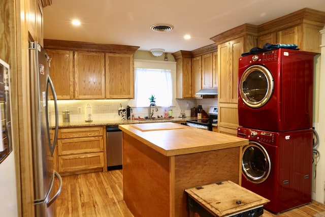 kitchen with stacked washer / dryer, backsplash, a center island, stainless steel appliances, and light wood-type flooring