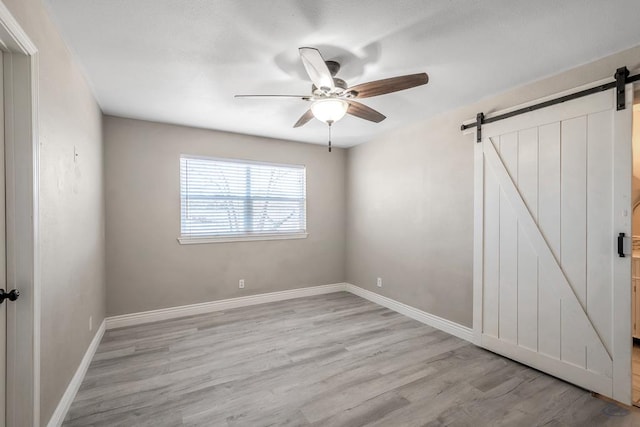 unfurnished bedroom featuring light hardwood / wood-style floors, a barn door, and ceiling fan