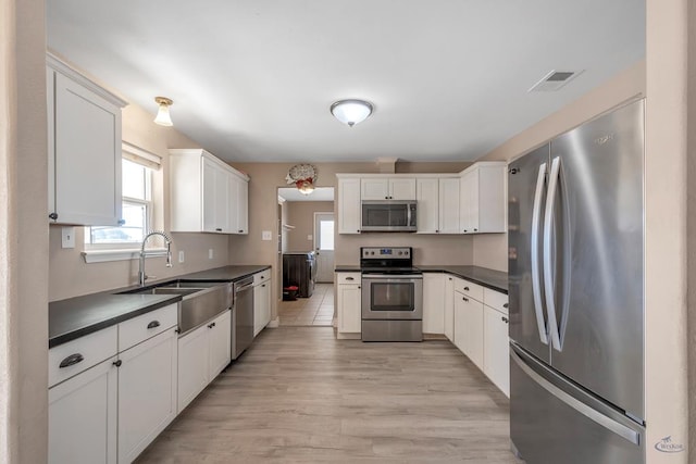 kitchen with stainless steel appliances, white cabinetry, sink, and light hardwood / wood-style flooring