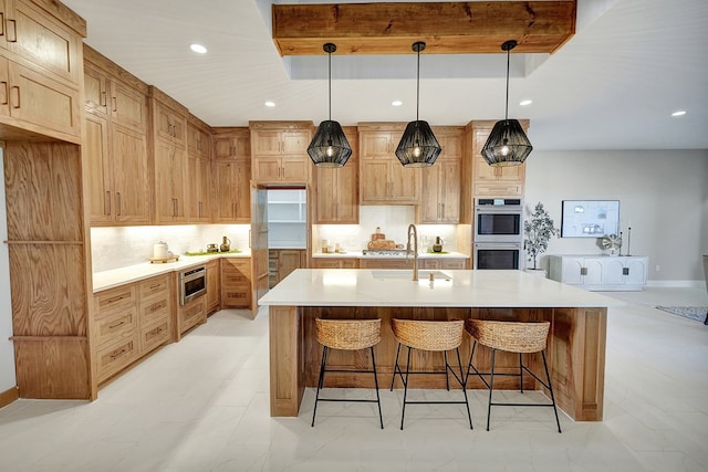 kitchen featuring sink, backsplash, stainless steel appliances, decorative light fixtures, and a large island with sink