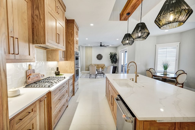 kitchen featuring appliances with stainless steel finishes, tasteful backsplash, an island with sink, sink, and hanging light fixtures