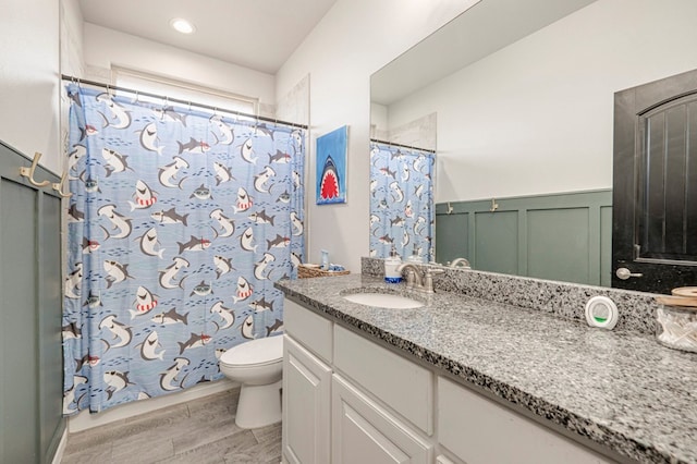 9 Senita Ct, Odessa, TX 79765 - bathroom with vanity, toilet, wood finished floors, a shower with curtain, and a wainscoted wall