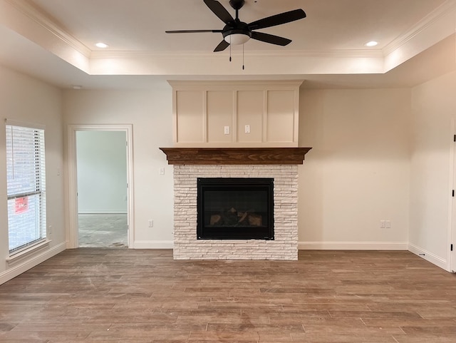 unfurnished living room featuring a tray ceiling, ceiling fan, a fireplace, and light wood-type flooring