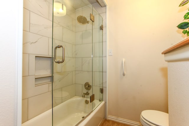 bathroom with baseboards, toilet, and shower / bath combination with glass door