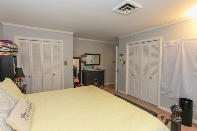 bedroom featuring visible vents, crown molding, baseboards, carpet floors, and multiple closets