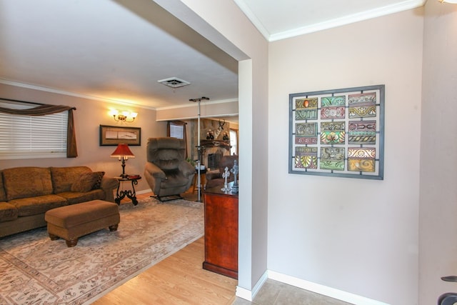living room featuring baseboards, ornamental molding, light wood finished floors, and visible vents
