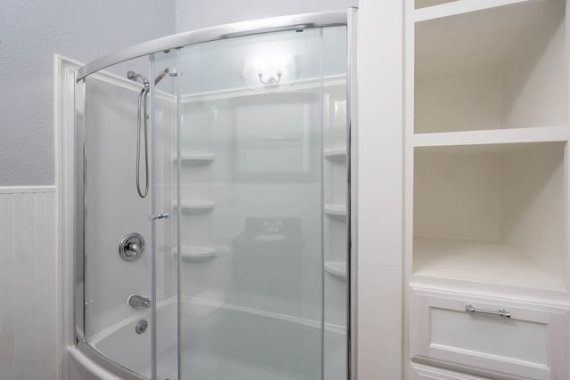 full bath with a wainscoted wall, a textured wall, and shower / bath combination with glass door