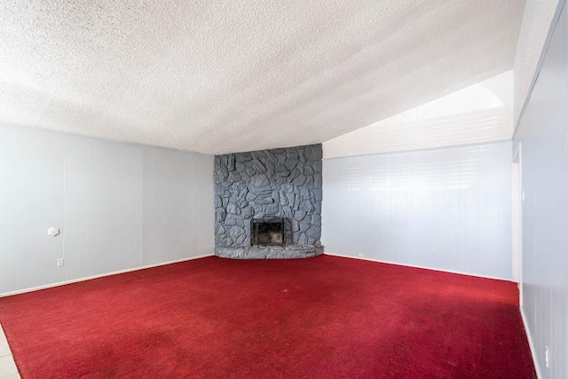unfurnished living room with a stone fireplace, vaulted ceiling, carpet flooring, and a textured ceiling