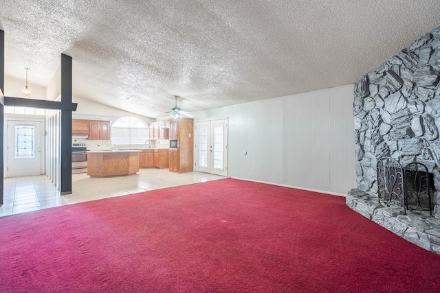 unfurnished living room featuring lofted ceiling, light colored carpet, light tile patterned floors, ceiling fan, and a stone fireplace