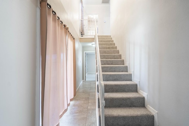 staircase featuring baseboards, visible vents, and a high ceiling