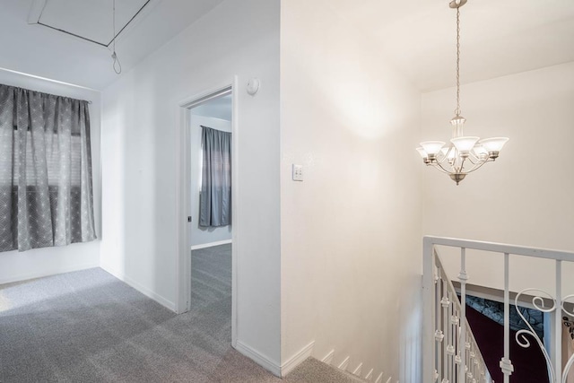 hall featuring an upstairs landing, carpet, baseboards, attic access, and a notable chandelier