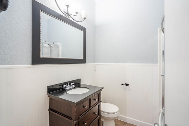 full bathroom featuring a wainscoted wall, a shower with door, toilet, and vanity