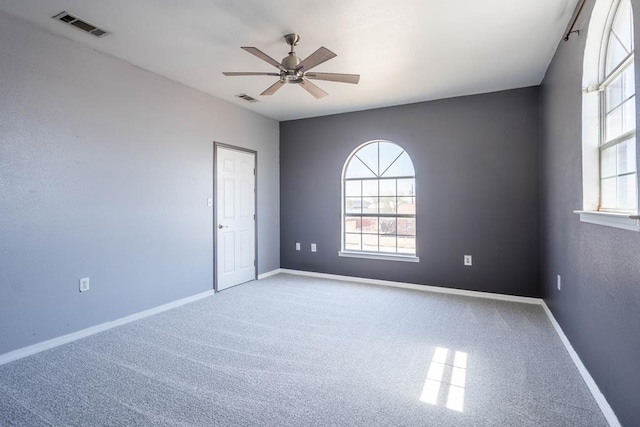 empty room featuring a wealth of natural light, ceiling fan, and visible vents