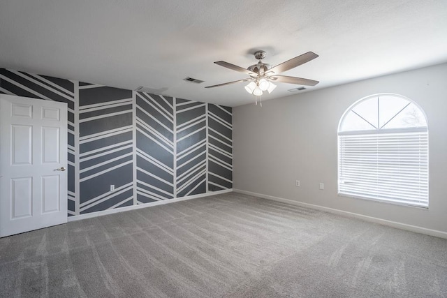carpeted spare room featuring baseboards, visible vents, and ceiling fan