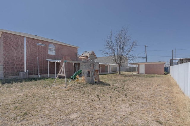 view of yard featuring fence, a storage shed, a playground, an outbuilding, and cooling unit