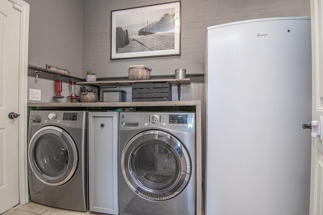 laundry area featuring washer and dryer, brick wall, and light tile patterned floors